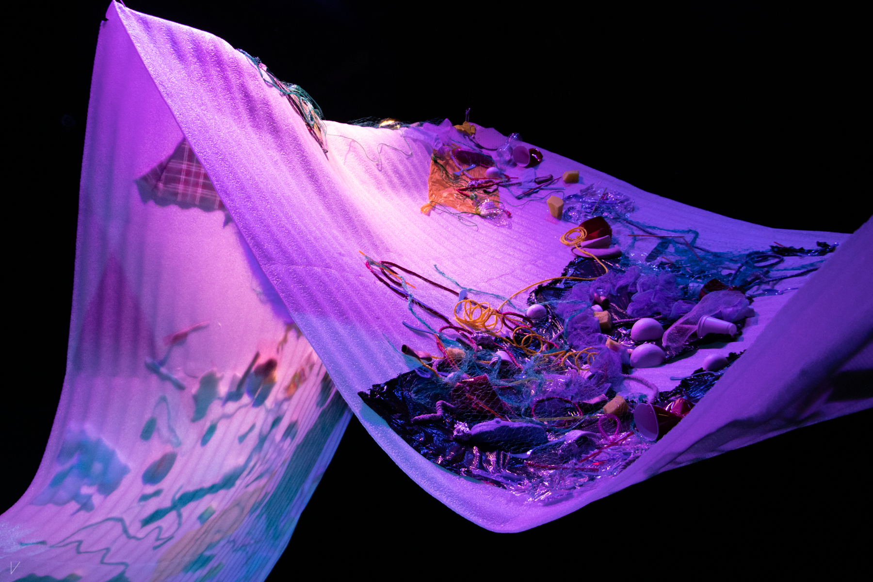 Drowning Voices set piece, a large swooping sheet of flexible styrofoam with garbage stuck to it, lit in purple and blue, from a medium distance