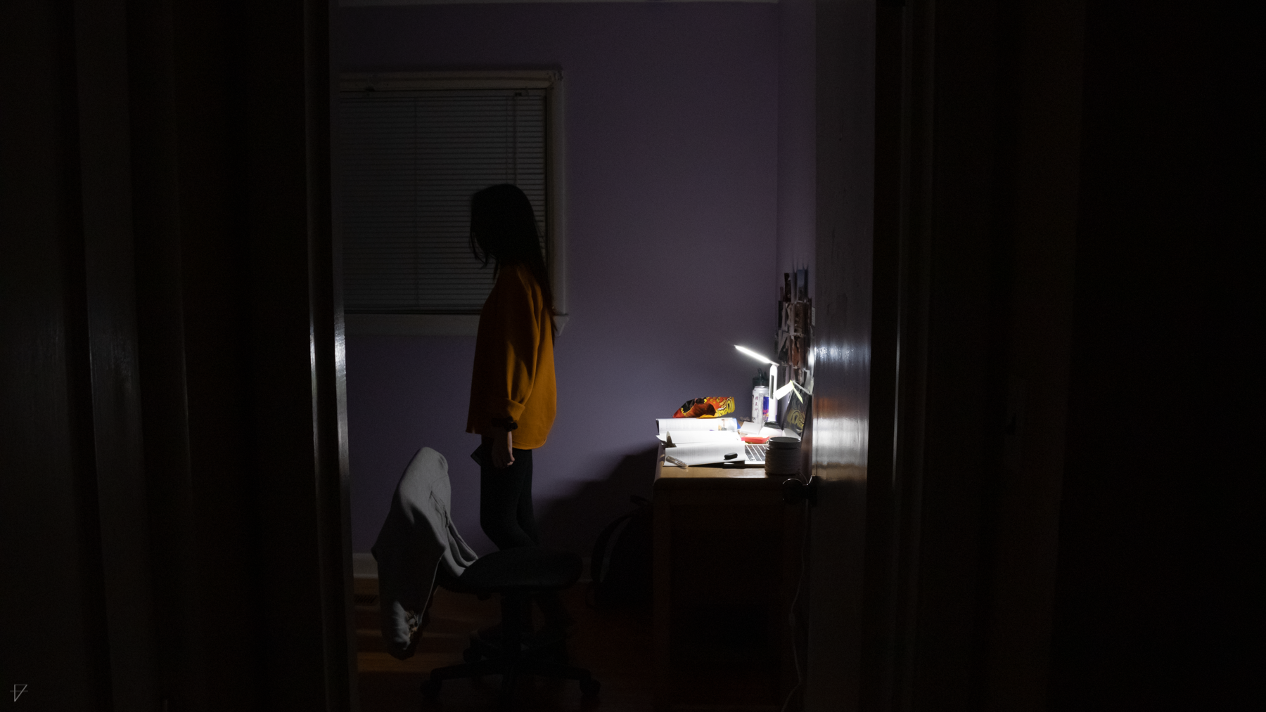 From the doorway a girl is seen walking away from her desk and laptop